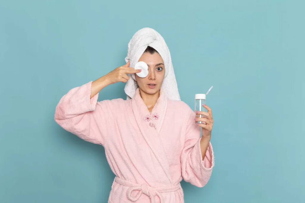 Woman in pink bathrobe applying skincare with a cotton pad