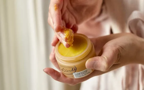 Hand scooping cleansing balm from a jar - Waterless Skincare: Benefits, Products & Sustainability - Zicail