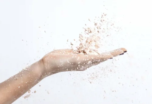 Hand tossing skincare powder into the air on white - Waterless Skincare: Benefits, Products & Sustainability - Zicail