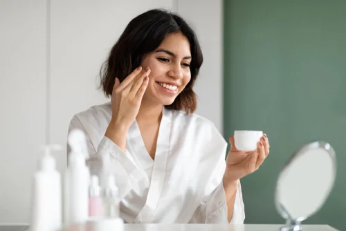 Woman applying Snail Mucin cream in front of mirror for skincare routine - Snail Mucin in Skincare: Benefits, Usage, and Advice - Zicail