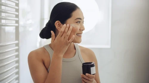 Woman applying cream to her face holding a jar - Waterless Skincare: Benefits, Products & Sustainability - Zicail