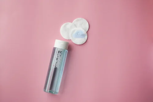 Micellar water bottle and cotton pads on a pink backdrop - Toner vs Essence: Differences & Which One You Need - Zicail Micellar water bottle and cotton pads on a pink backdrop - Toner vs Essence: Differences & Which One You Need - Zicail