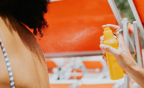 Person spraying sunscreen on anothers back in the sun - Sunscreen Stick vs. Spray: Key Differences & Use Cases 2026 - Zicail Person spraying sunscreen on anothers back in the sun - Sunscreen Stick vs. Spray: Key Differences & Use Cases 2026 - Zicail