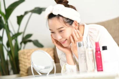 Woman admiring her reflection surrounded by skincare products - Toner vs Essence: Differences & Which One You Need - Zicail Woman admiring her reflection surrounded by skincare products - Toner vs Essence: Differences & Which One You Need - Zicail
