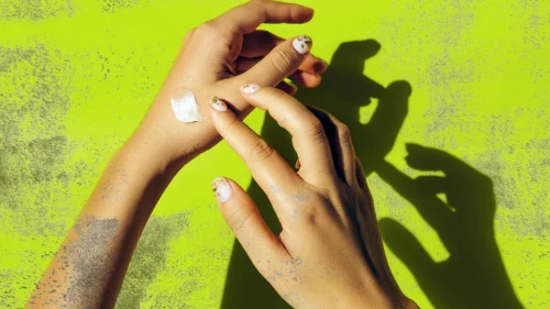 Hands applying a dab of lotion on a neon green background - Is Sunscreen Gluten-Free? Safe Options & Key Ingredients 2026 - Zicail Hands applying a dab of lotion on a neon green background - Is Sunscreen Gluten-Free? Safe Options & Key Ingredients 2026 - Zicail