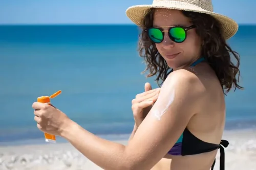 Woman in a hat applying sunscreen by the ocean - Natural Skincare Routine: Simple Steps for Healthy Skin [October 2026] - Zicail