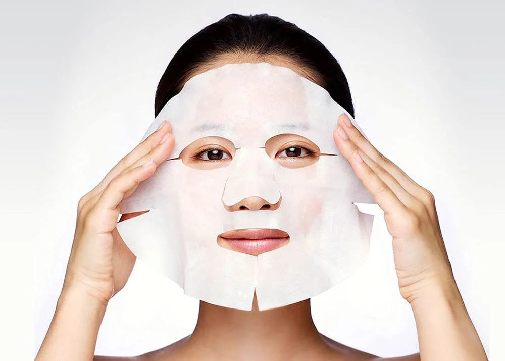 Woman positioning a white sheet mask on her face