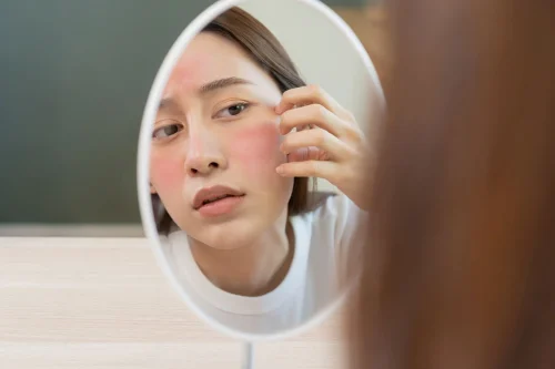 鏡で顔の赤みをチェックする女性 - スキンケアにおけるポリグルタミン酸：保湿とアンチエイジング 2026 - Zicail