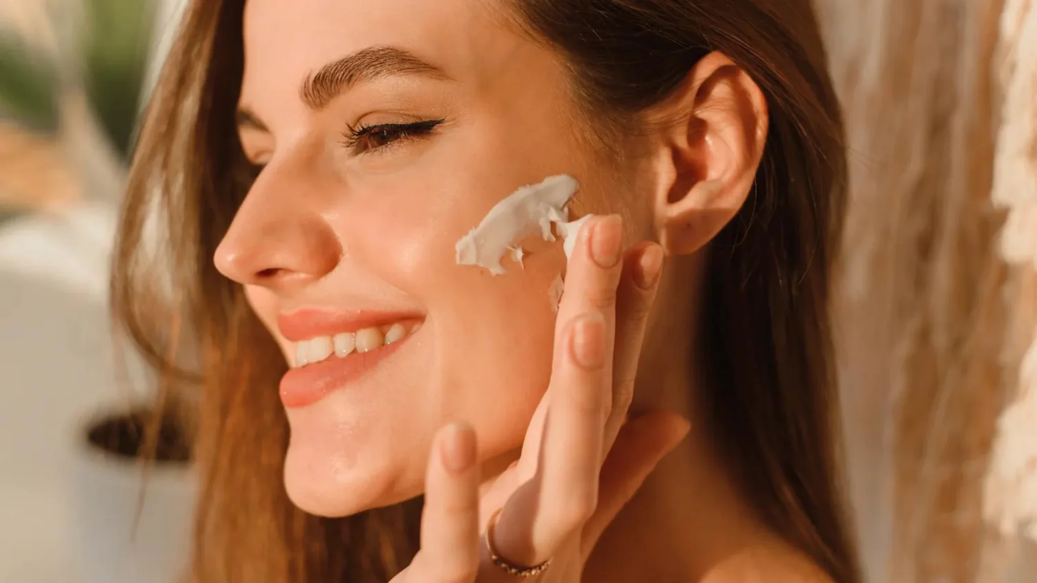 Smiling woman applying cream to her cheek in natural light