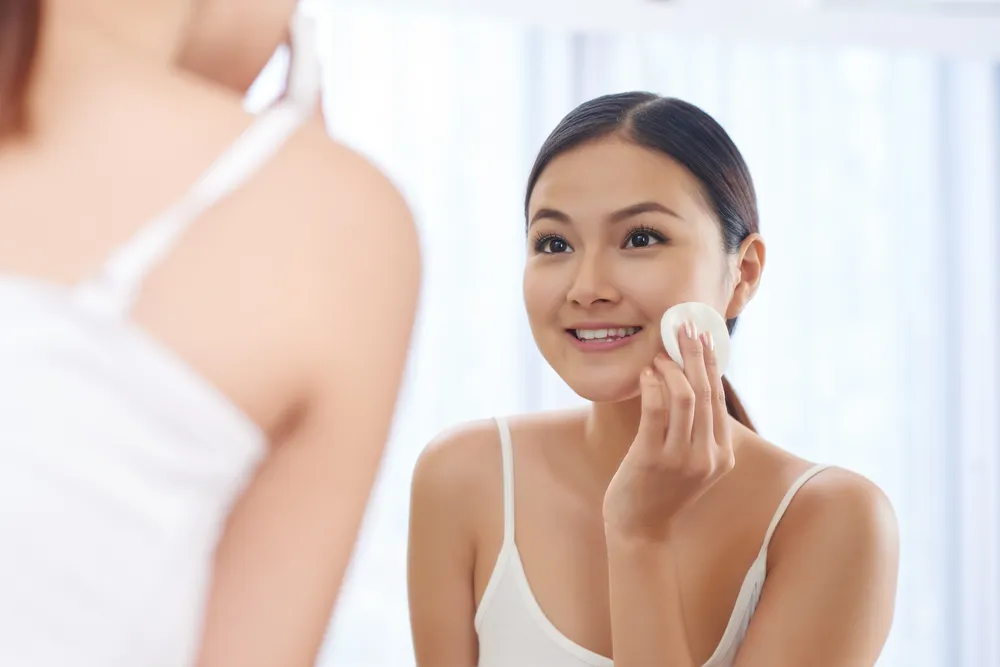 Smiling woman applying toner with cotton pad in front of mirror - Daily Toner Side Effects: Safe or Harmful Use? 2026 - Zicail Smiling woman applying toner with cotton pad in front of mirror - Daily Toner Side Effects: Safe or Harmful Use? 2026 - Zicail