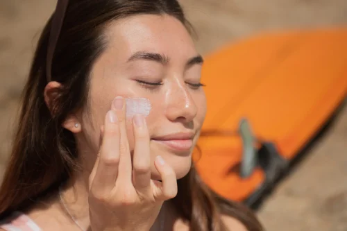 Woman applying sunscreen on her face outdoors - Does High SPF Sunscreen Protect You Better? 2026 - Zicail