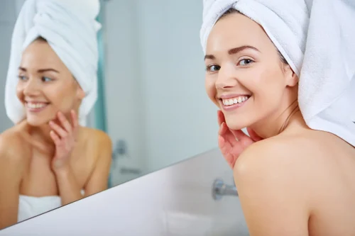 Woman in a towel smiling at her reflection embracing her skin - How to Layer Skincare: A Rule-Based Guide to Correct Order 2026 - Zicail