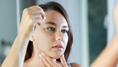 A woman applies makeup while gazing into a mirror - Is Vitamin C Good Under Makeup? Tips for Glowing Skin 2026 - Zicail