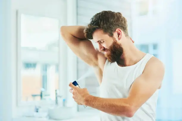 男性が浴室で脇の下に制汗剤をスプレーしている - 制汗剤と制汗剤：主な違いと用途 2026 - Zicail