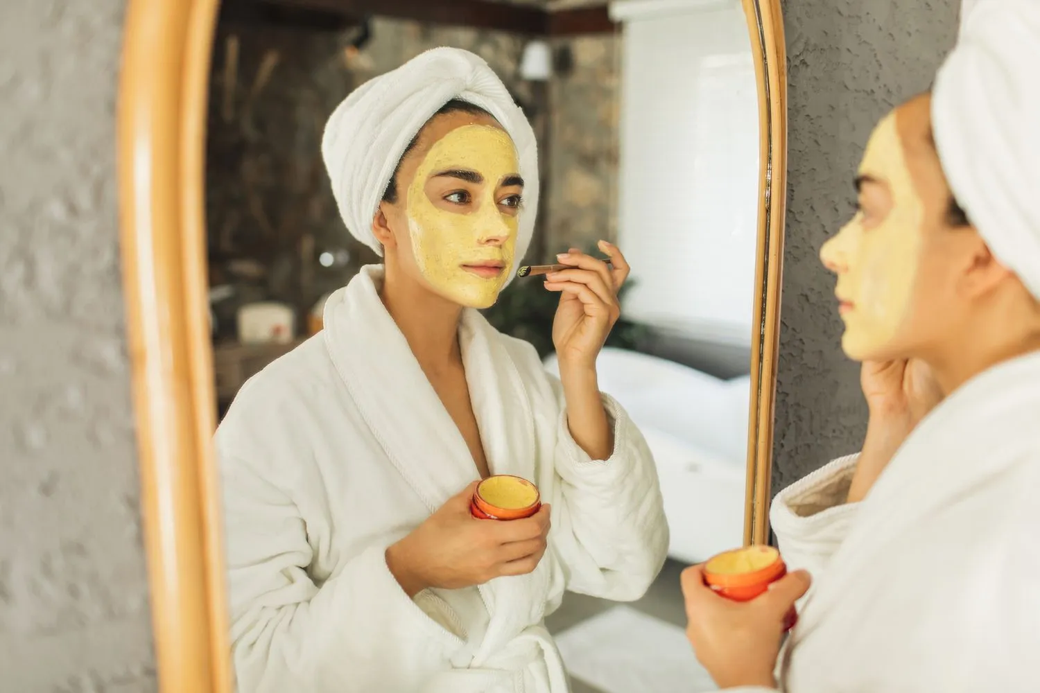 A woman applying a turmeric face mask in front of a mirror - Turmeric for Skin: Benefits, Uses, and Safety Tips 2026 - Zicail