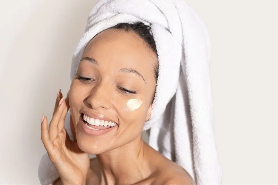 Woman applying skincare product to her face after a shower - Beta-Glucan in Skincare: Benefits & How to Use It 2026 - Zicail