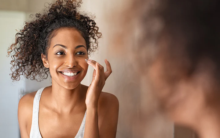 Woman smiling while applying face cream in the mirror - Xylitol in Skincare: Hydration, Benefits & Uses Explained 2026 - Zicail