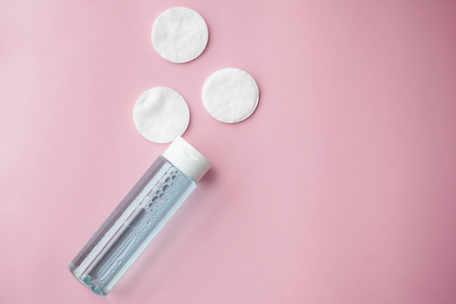 Toner bottle with cotton pads on pink background skincare toner and facial cotton pads arranged in a minimal flat lay representing post cleansing hydration step - Do You Need a Toner? Decide If You Can Skip It Now 2026 - Zicail