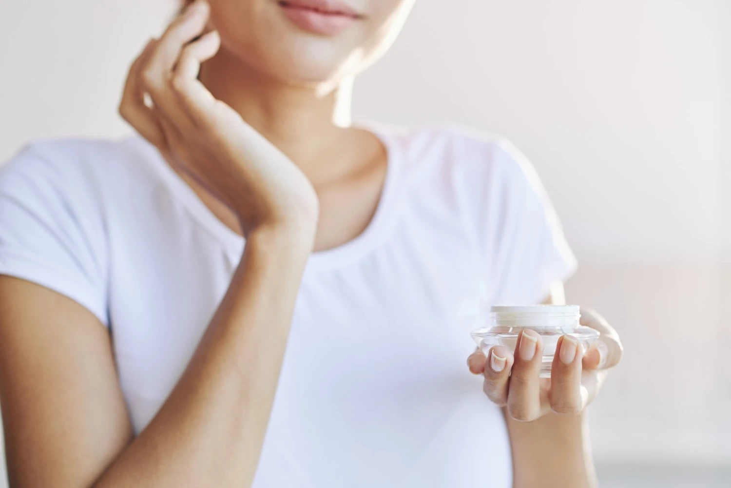 女性がクリーム状の保湿剤を顔に塗っている様子（瓶を開けたまま） - ジェルタイプとクリームタイプの保湿剤：どちらが肌に良い？ 2026 - Zicail
